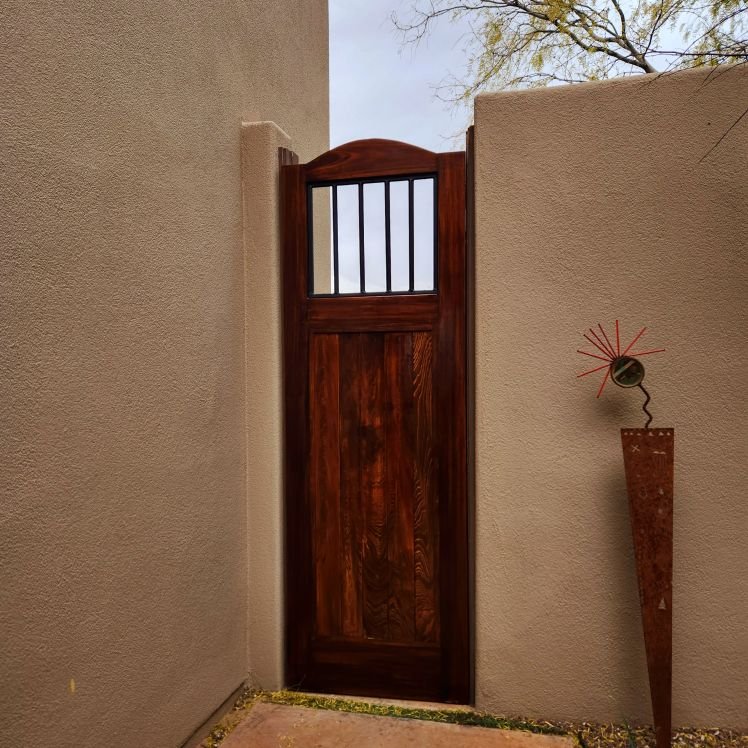 Arched stained wood courtyard gate with iron-barred window set in a stucco wall