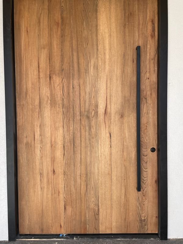 Custom flat-panel hardwood pivot entry door with a long black pull
