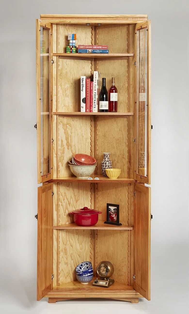 Cypress corner cabinet with glass doors holding books, bowls, and bottles